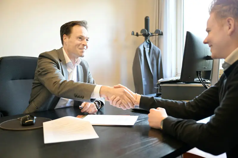 Twee mannen schudden elkaar de hand over een bureau